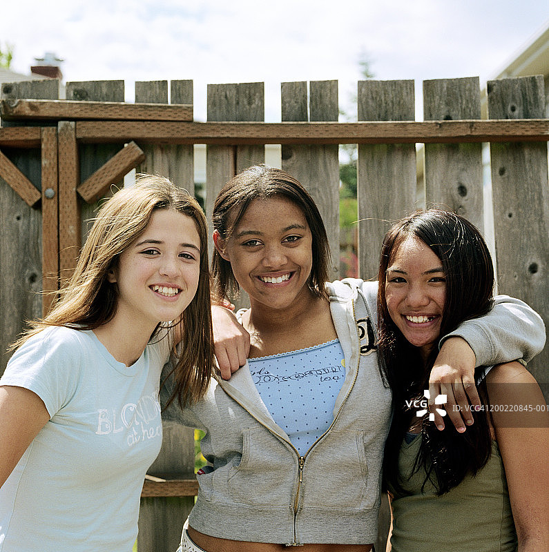 三个十几岁的女孩(12-14岁)站在栅栏旁，微笑着，像图片素材