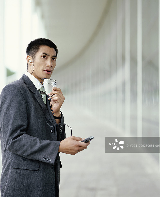 在大楼外使用手机时戴耳机的商人图片素材