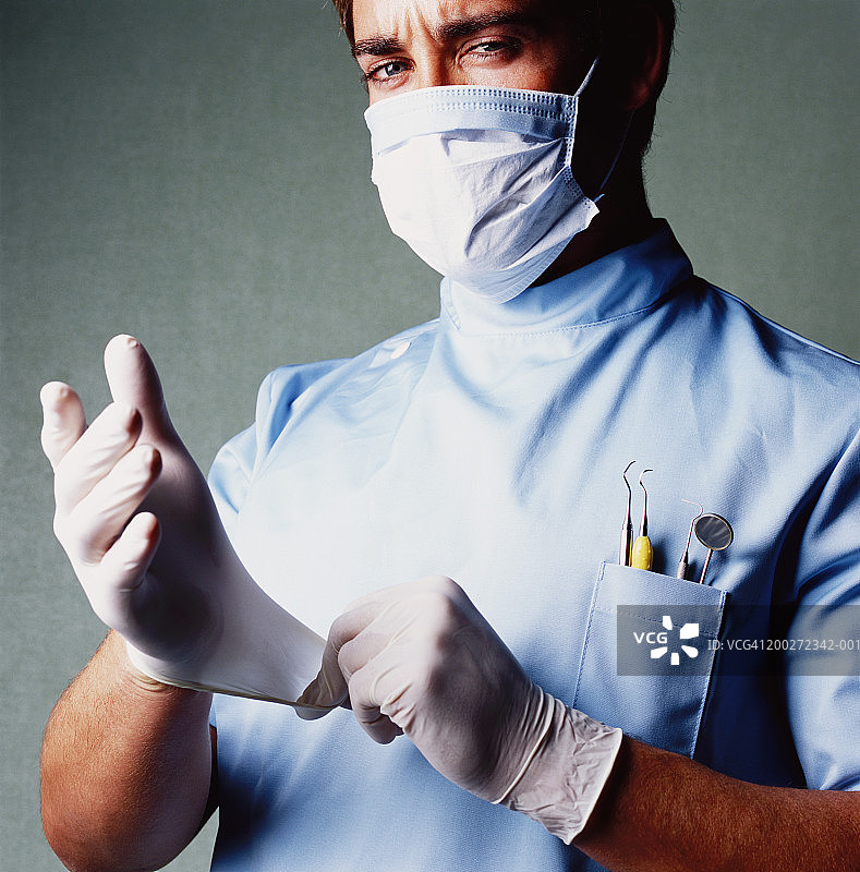 年轻男牙医戴上手术手套，戴上口罩，画像图片素材