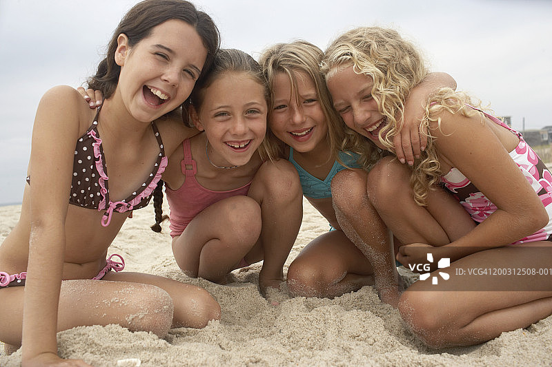 四个女孩(8-12岁)在海滩上挤在一起，笑着，像图片素材