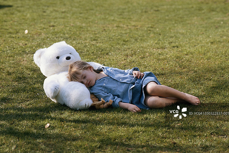 女孩(4-5)和泰迪熊在草地上睡觉图片素材