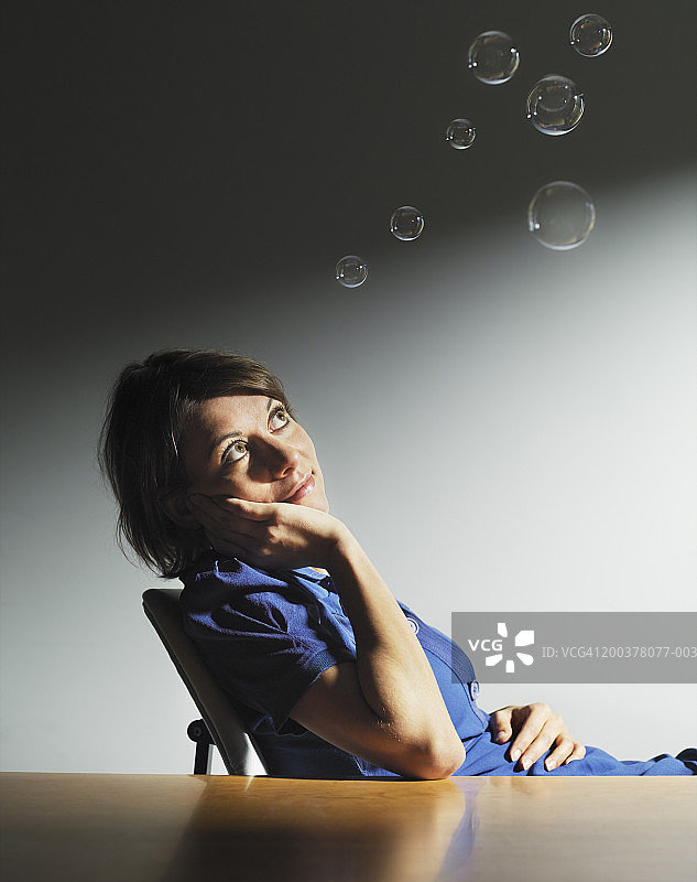 女人坐在桌前看着泡泡，手捧脸颊，微笑着图片素材