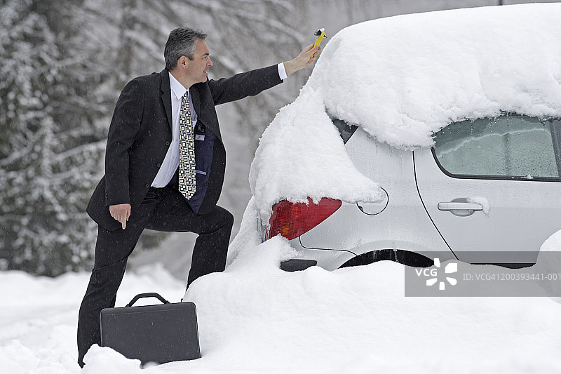 穿西装的男人从车上刮雪，侧视图图片素材