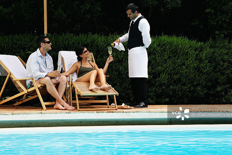 男服务员给情侣端香槟，泳池对面的景色图片素材