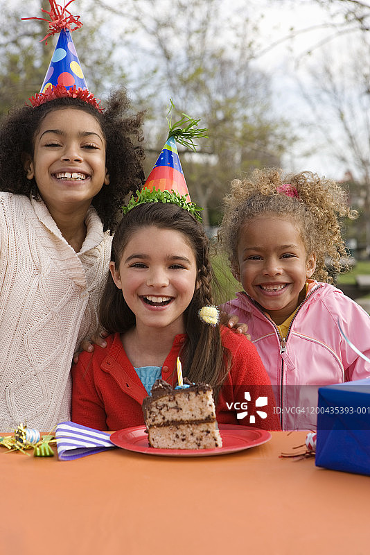 女孩(5-10人)戴着派对帽，桌上放着一块蛋糕图片素材