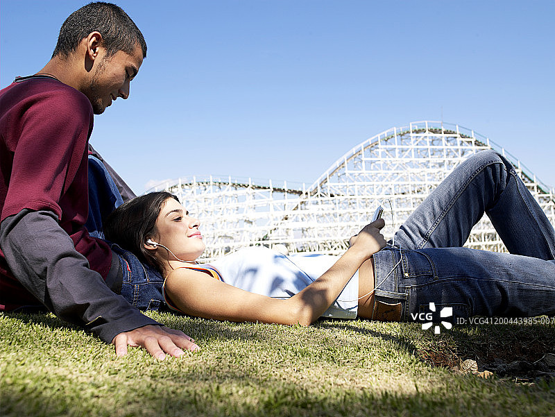 一对年轻夫妇在游乐场的草坪上，女人拿着MP3图片素材