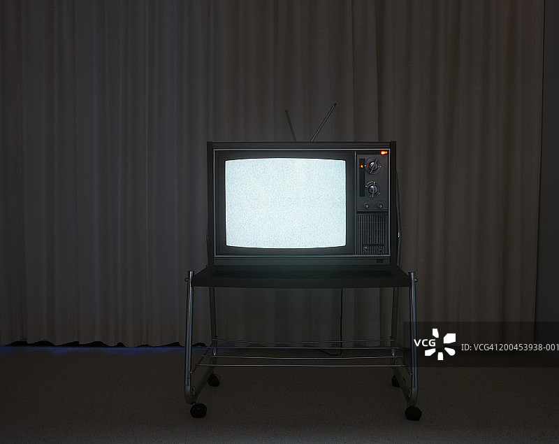在黑暗的房间里，窗帘前的架子上放着旧电视图片素材