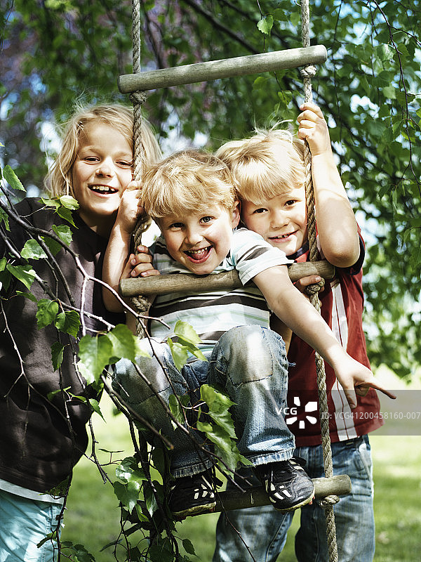 三兄弟(4-9)在花园里的绳梯上，面带微笑，画像图片素材