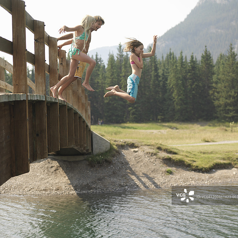 父亲和女儿(8-11)从桥上跳入水中，侧视图图片素材