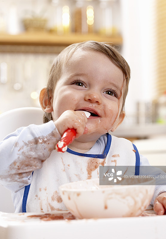 男婴(9-12个月)裹着盛满食物的碗，面带微笑图片素材
