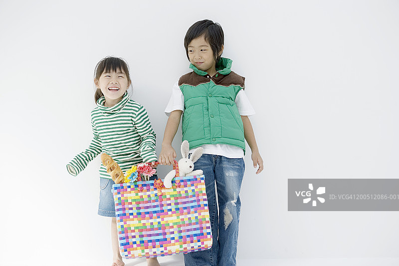 男孩(4-6)和女孩(3-5)拿着装满玩具的彩包，微笑着图片素材