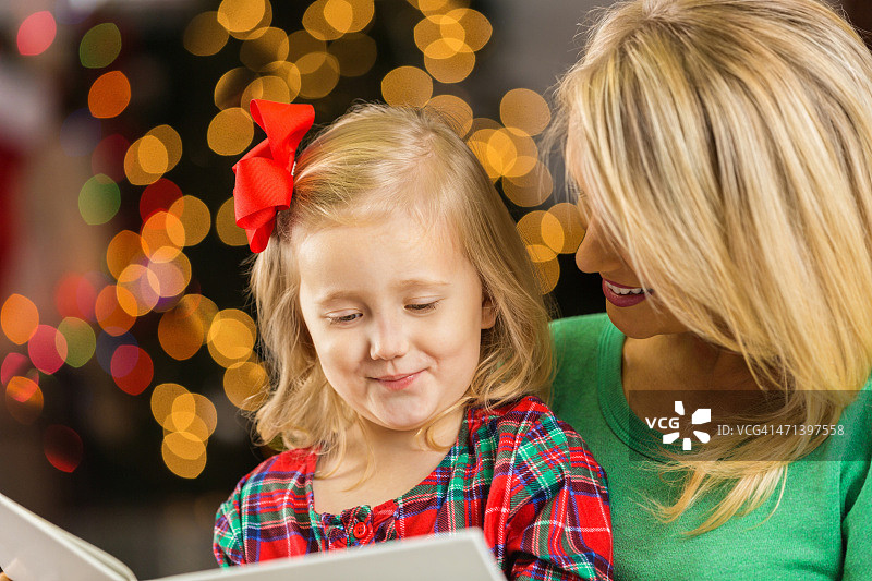 可爱的女孩在圣诞节前夕和妈妈一起读睡前故事图片素材