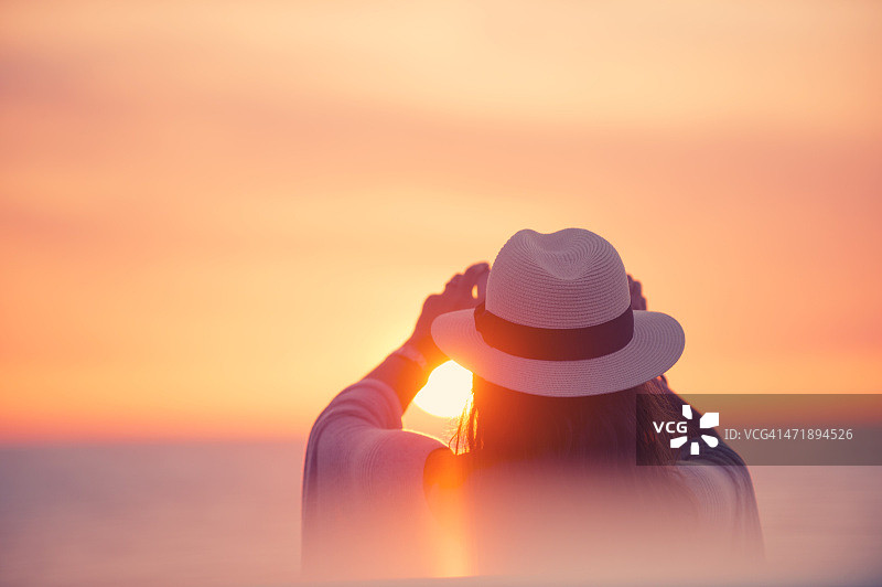 成熟的女人在日落时用手机拍照。图片素材