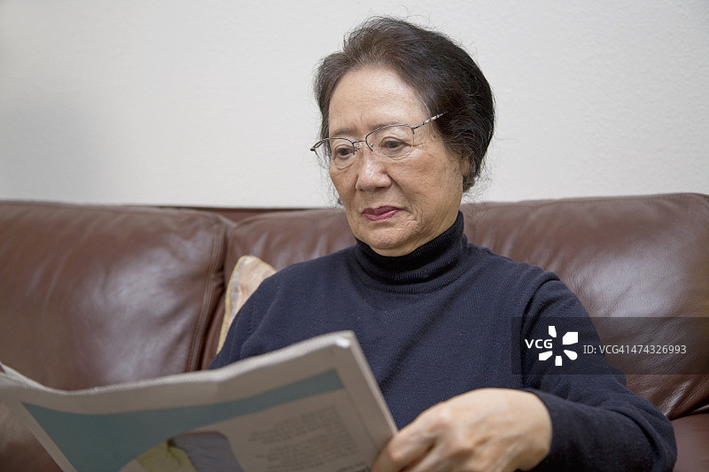 年长的韩国亚裔妇女在看报纸图片素材