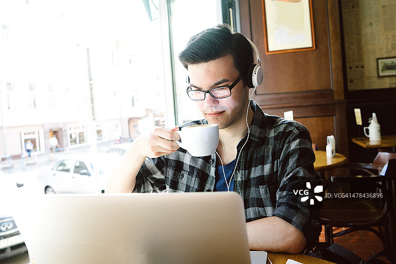 一个愉快的年轻人在咖啡店里使用笔记本电脑图片素材