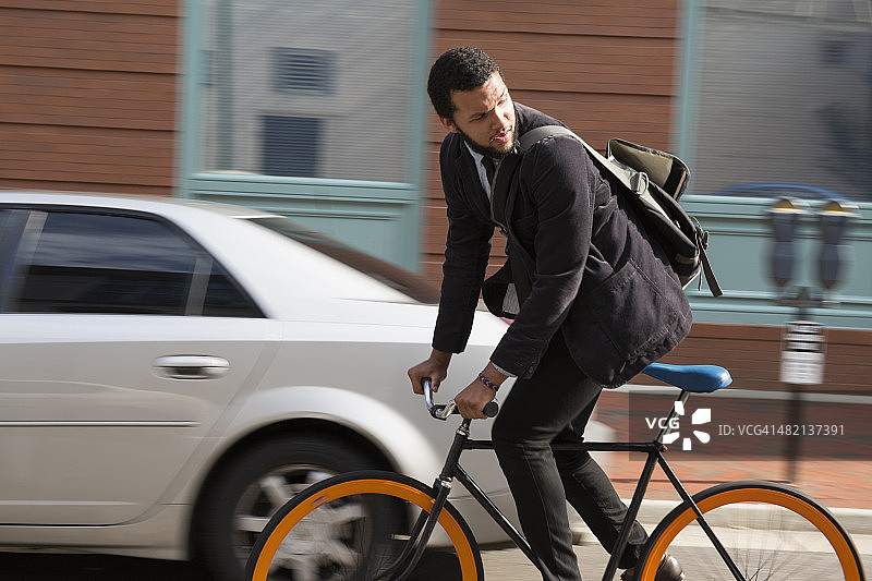 在城市街道上骑自行车的混合种族商人图片素材