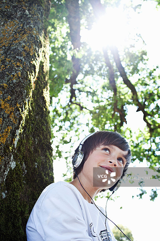 男孩戴着耳机靠在树上图片素材