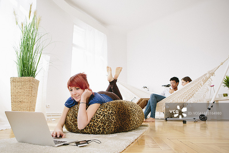 年轻的红发女人和朋友在吊床上玩笔记本电脑图片素材