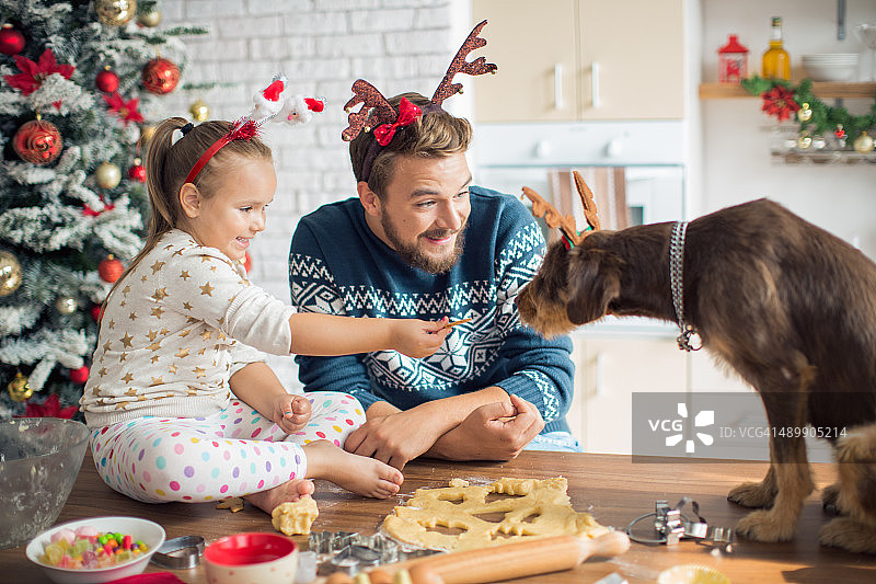 父亲和女儿在厨房和他们的狗过圣诞节。图片素材