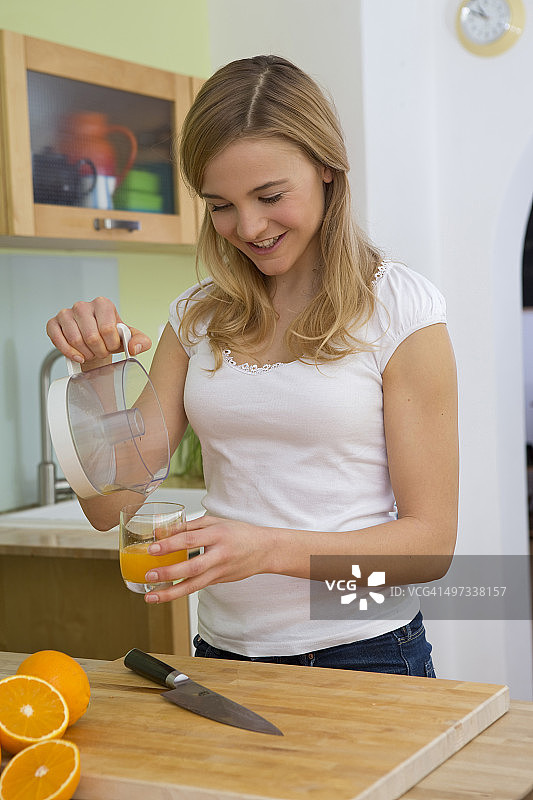 年轻女子把橙汁倒进玻璃杯里图片素材