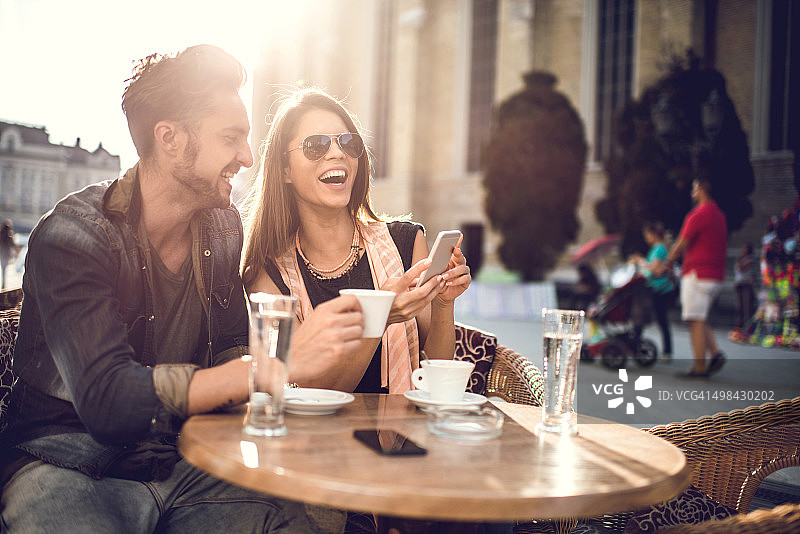 一对愉快的夫妇在咖啡馆里放松，使用智能手机。图片素材