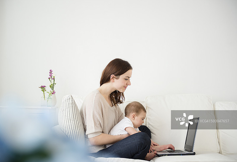 母亲和婴儿在沙发上使用笔记本电脑图片素材