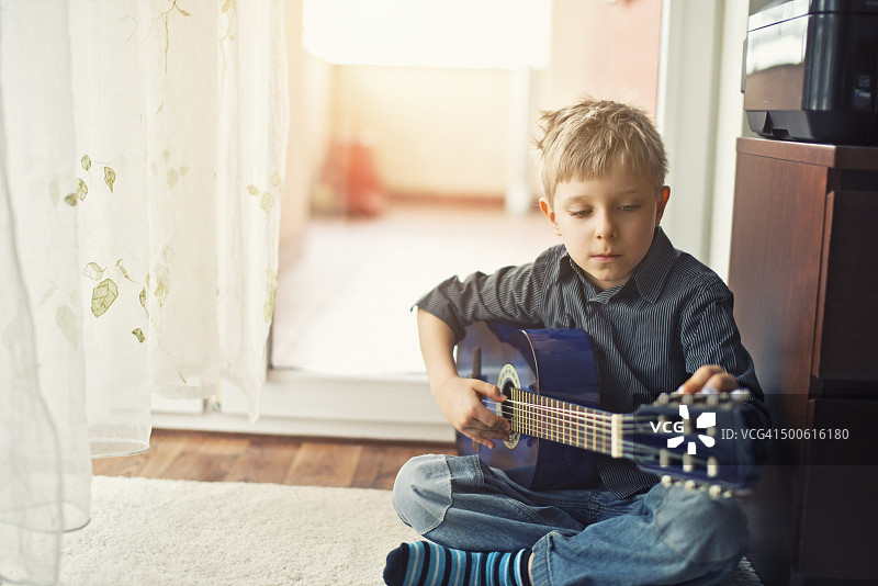 小男孩在调他的蓝色原声吉他。图片素材