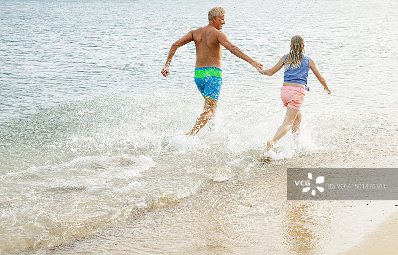 父亲和女儿在沙滩上牵着手奔跑图片素材
