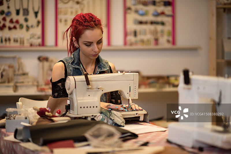 梳着脏辫在缝纫机上工作的女裁缝。图片素材