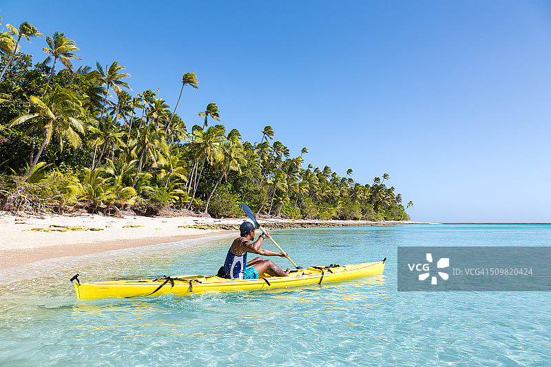 一名男子在斐济热带岛屿附近的海滩上划皮艇图片素材