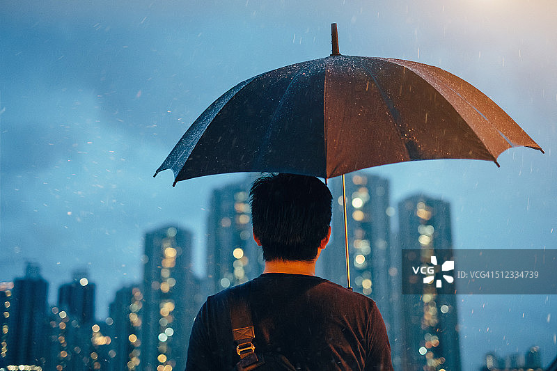 年轻的男性拿着伞看着城市图片素材