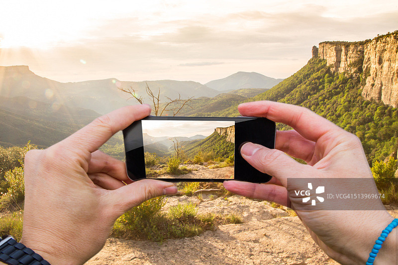 一名男子用智能手机从个人角度拍摄了日出时美丽的山谷和峭壁。图片素材