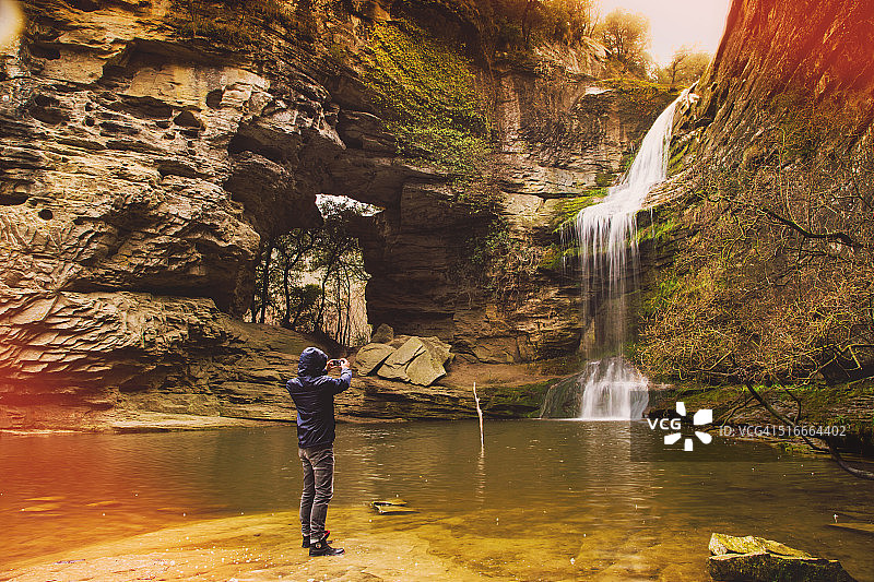 一个徒步旅行者在一个令人惊叹的马尾瀑布前用智能手机拍照，在独自的自然探险之旅中。图片素材