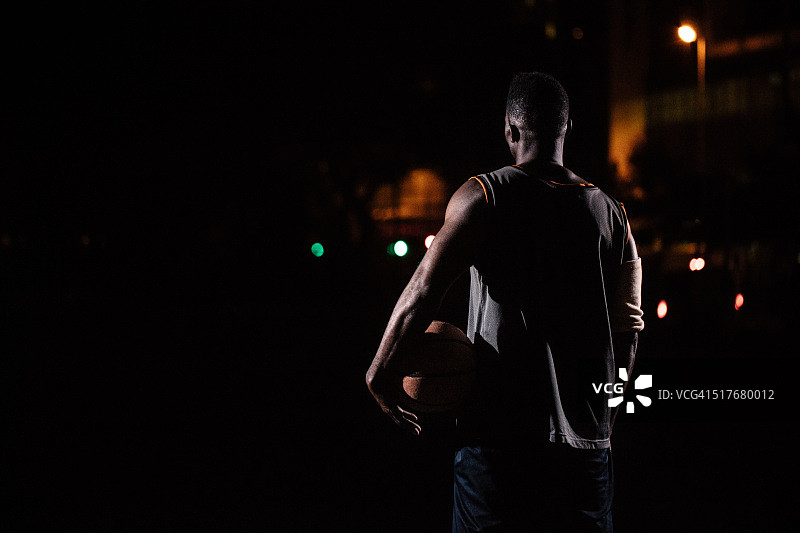篮球运动员抱着篮球的臀部在晚上图片素材