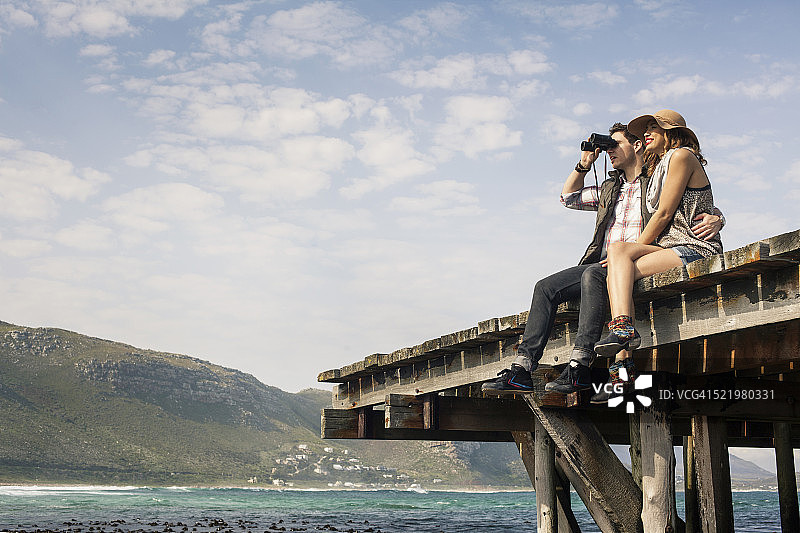 年轻夫妇坐在老码头边用望远镜看，开普敦，西开普，南非图片素材