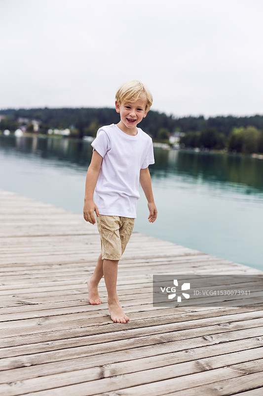 微笑的小男孩走在码头在一个湖的肖像图片素材