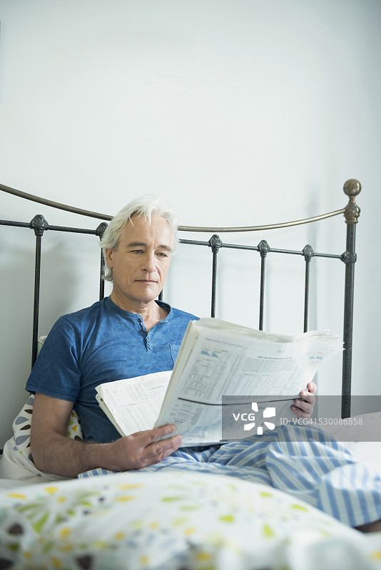 一个成熟的男人坐在床上看报纸图片素材