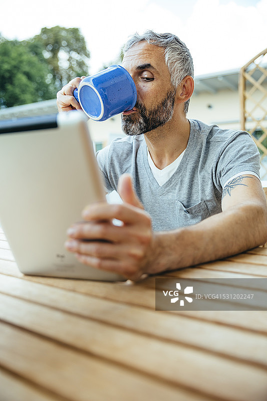 男子坐在阳台上用平板电脑喝咖啡的肖像图片素材