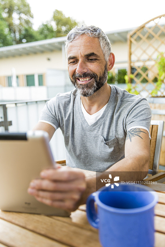 微笑的男子坐在阳台上使用平板电脑的肖像图片素材