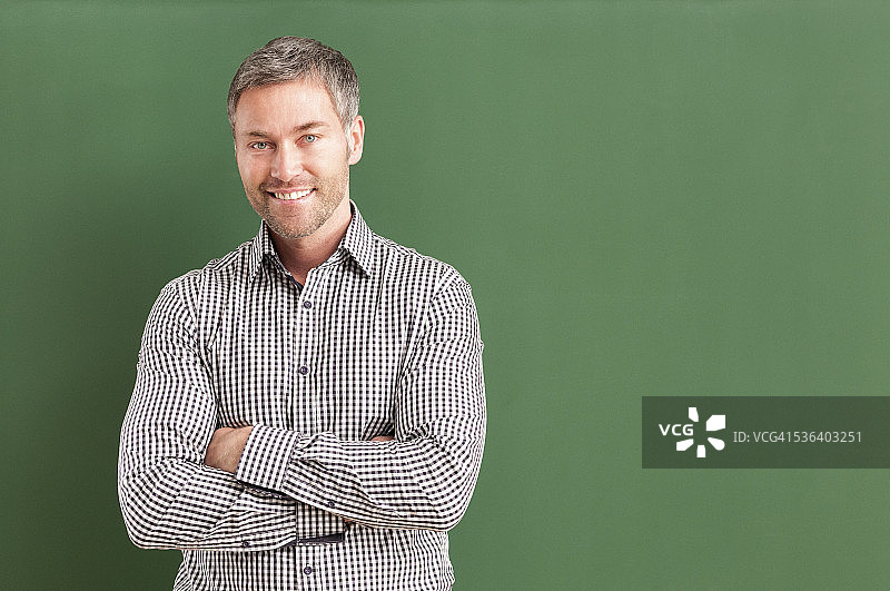 微笑的老师双臂交叉站在黑板前图片素材