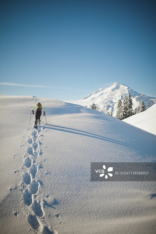一个穿雪鞋的人走过积雪覆盖的山脊线。图片素材