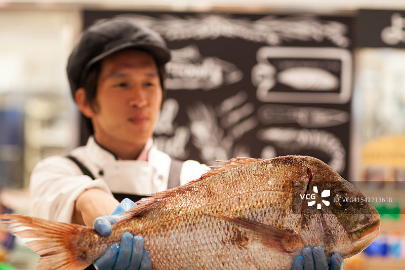 鱼贩子在超市的海鲜区举起一条鱼图片素材
