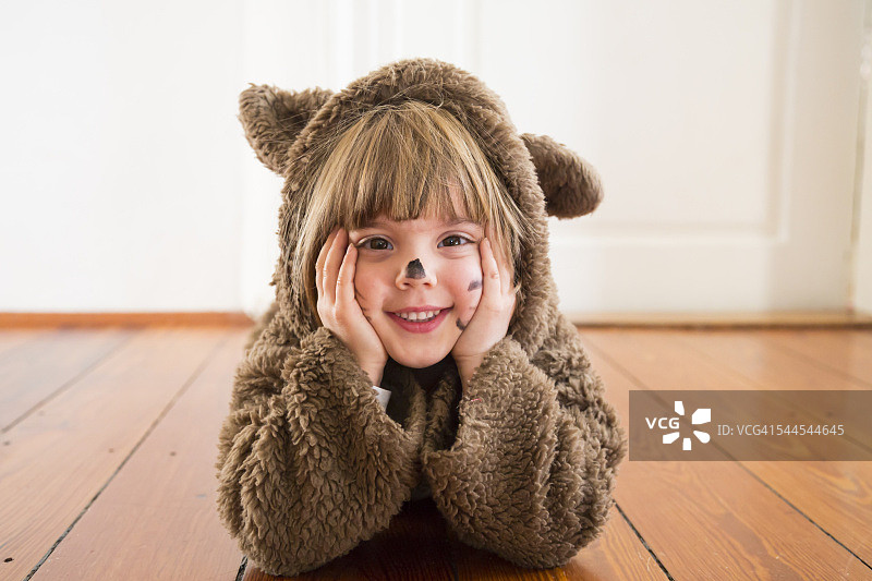 快乐的小女孩伪装成一只熊躺在木地板上的肖像图片素材
