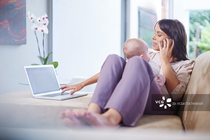 妈妈抱着宝宝坐在沙发上，一边用笔记本电脑工作，一边打手机图片素材