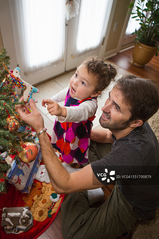 父亲和女儿在圣诞树上放置圣诞装饰品图片素材