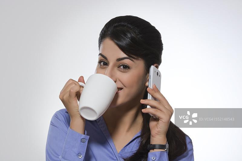 肖像美丽的女商人使用电话，而有咖啡对灰色的背景图片素材