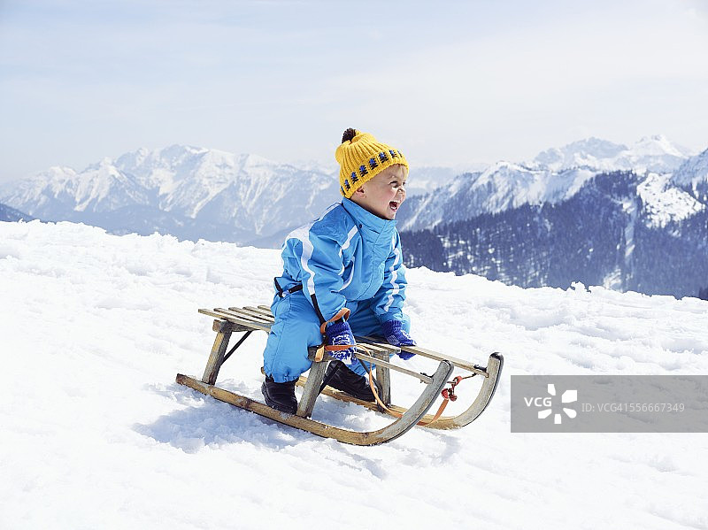 德国，泰根塞，瓦尔贝格，坐在雪橇上微笑的小男孩图片素材