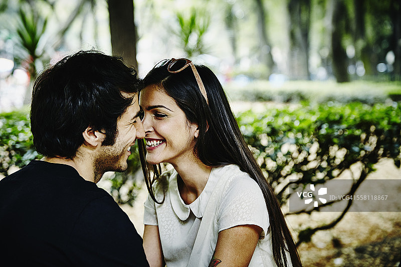 一对微笑的情侣坐在公园里，倾身亲吻图片素材