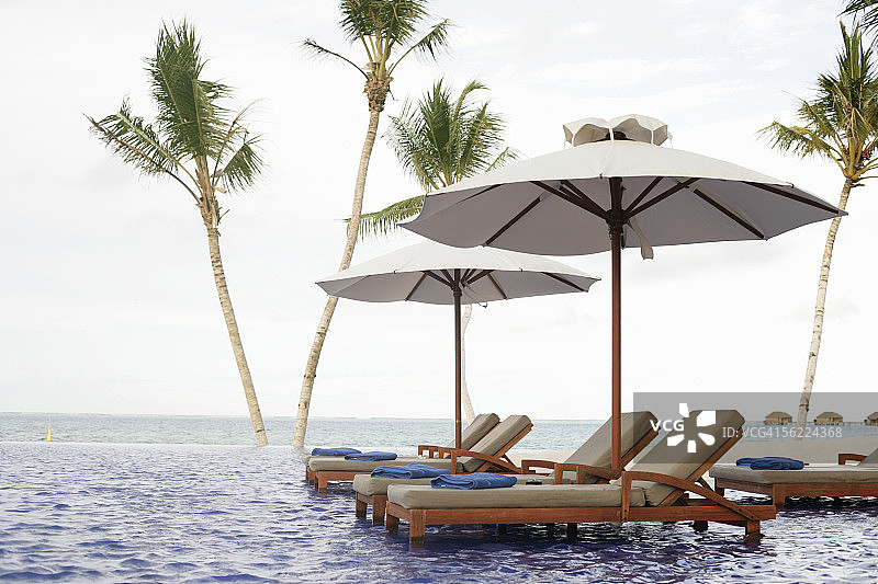 浅水里放着躺椅和遮阳伞，背景是棕榈树图片素材