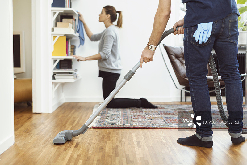 低部分的男人吸尘地板，而女人清洁货架在家里的背景图片素材